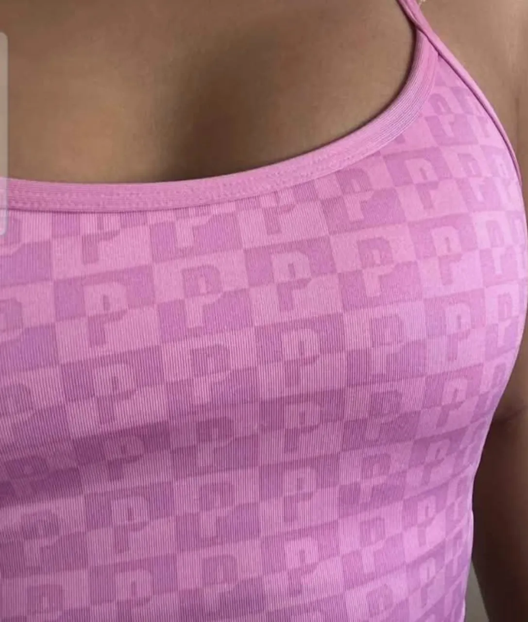 Top deportivo rosa con estampado de cuadros y logo 'P' repetido. Posee tiras finas cruzadas en la espalda.