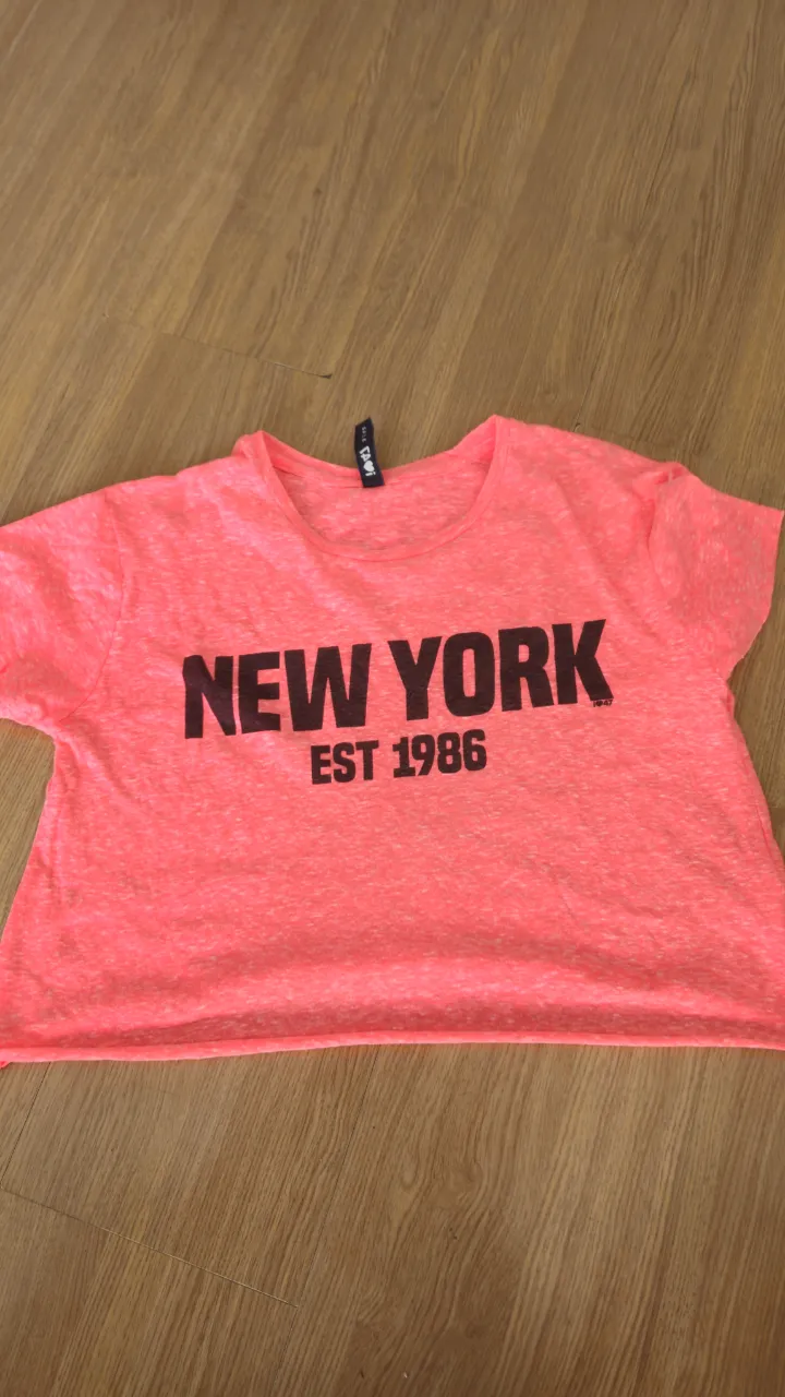 Remera crop de color rosa neón con estampado "NEW YORK EST 1986" en negro. Ideal para un look casual y moderno.