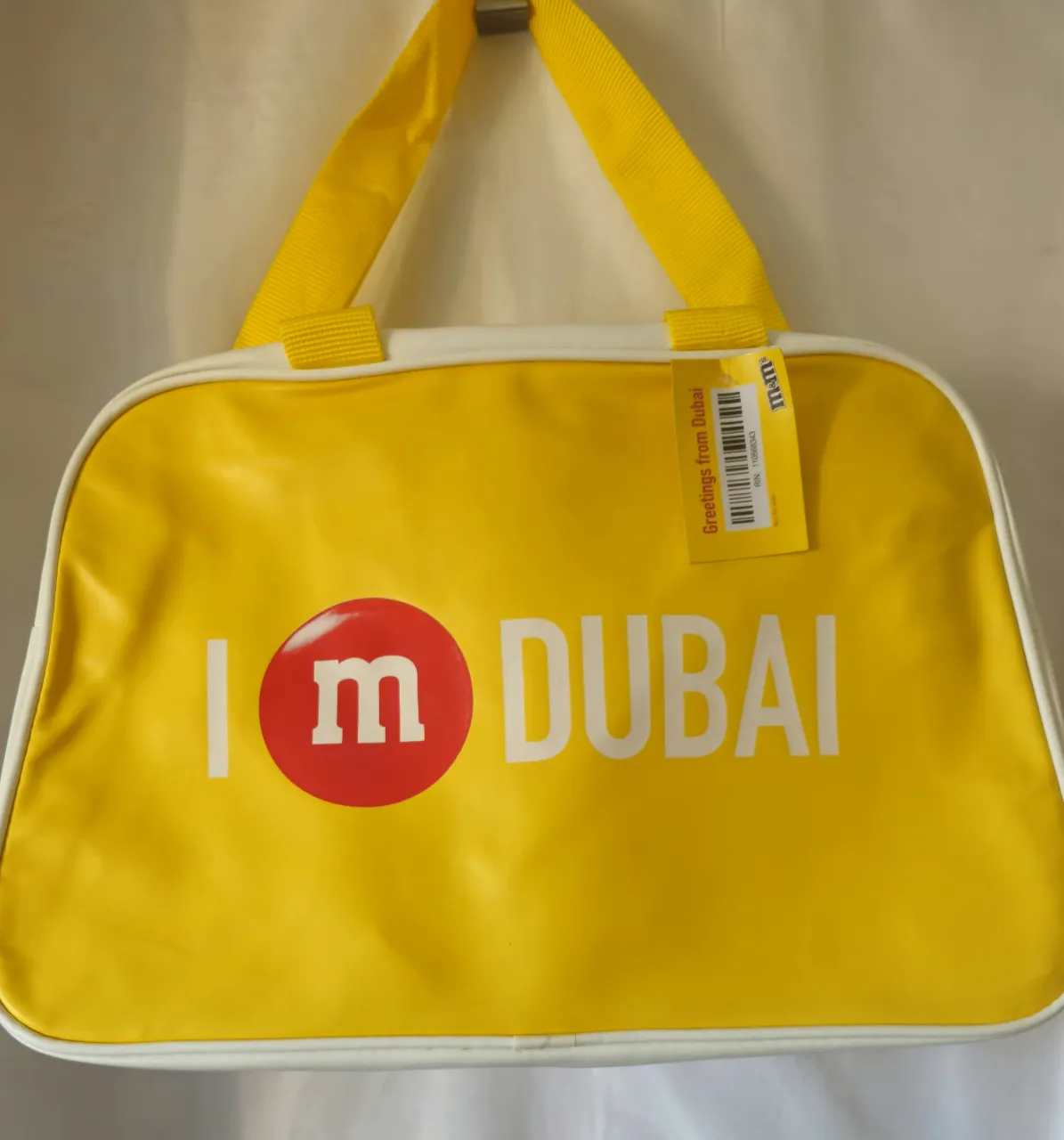 Bolso deportivo amarillo con detalles blancos, con el logo de M&M's y la frase 'I Dubai'. Ideal para llevar tus cosas al gimnasio o para un viaje corto.Medida 45*30*16 cm .
