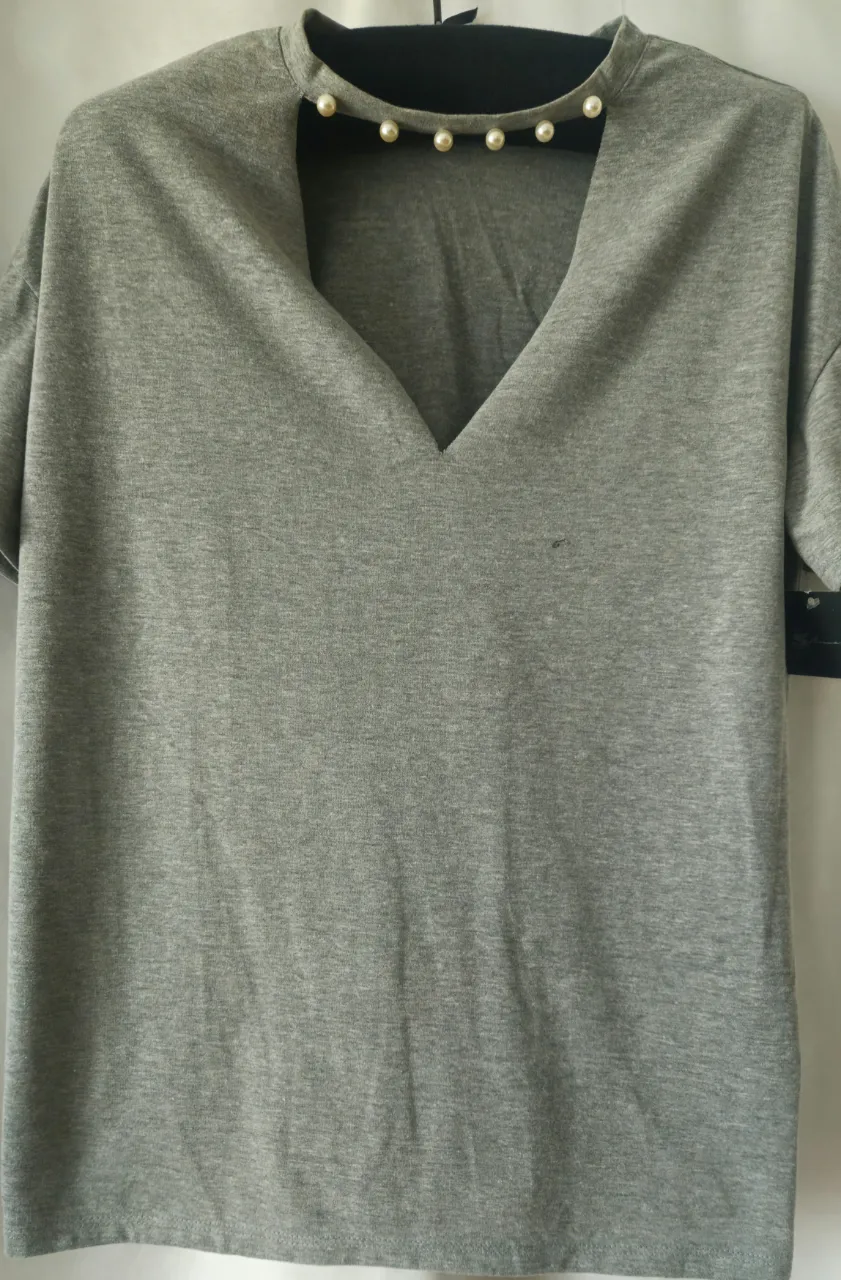 Remera gris con detalle de perlas en el cuello. Corte en V y mangas cortas. Ideal para un look casual y moderno.