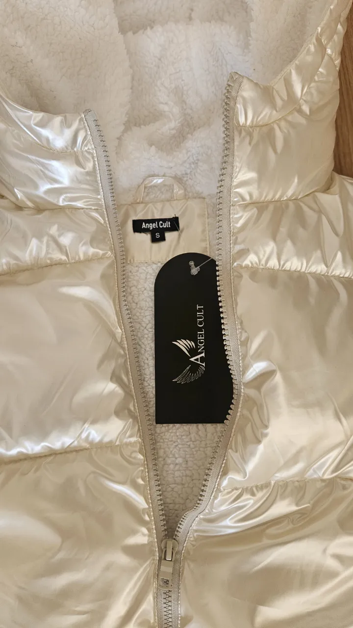 Chaleco acolchado de mujer, color blanco perlado, con capucha y forro de piel sintética. Cierre con cremallera y etiqueta de la marca Angel Cult. Ideal para el invierno.