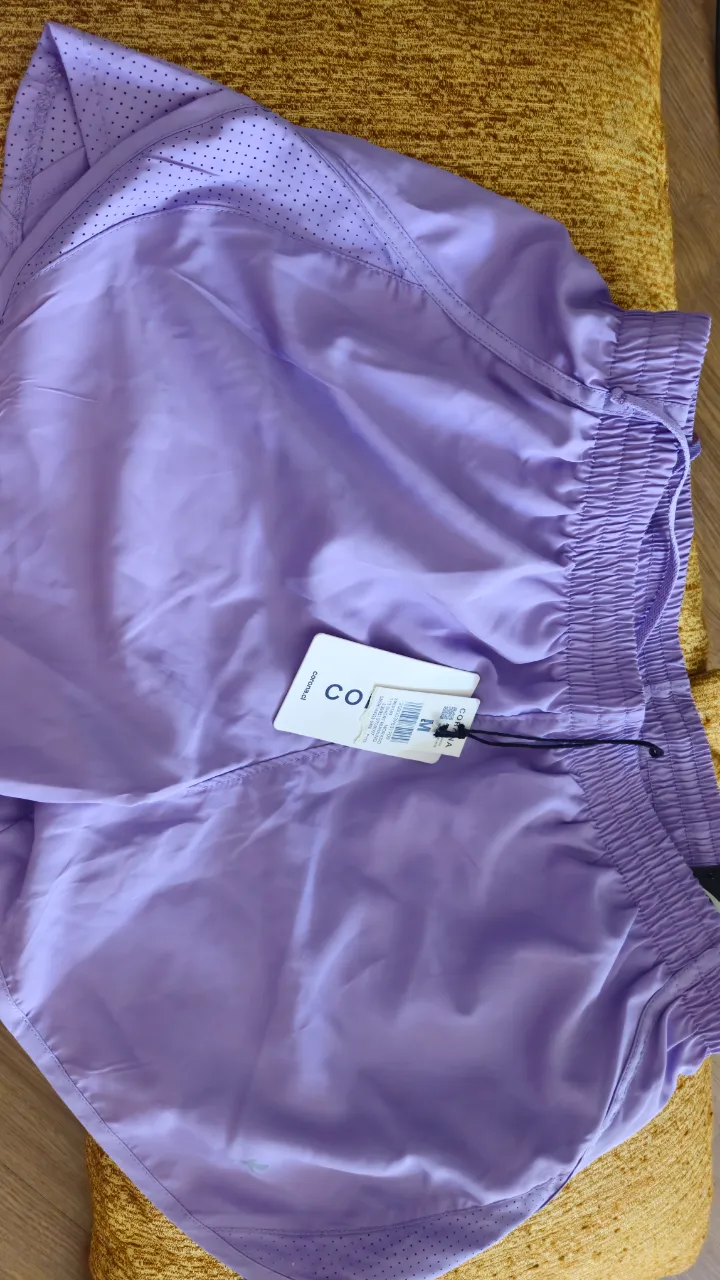 Shorts deportivos de color lila, ideales para entrenar o para un look casual y cómodo. Tienen detalles de perforaciones y un diseño moderno.