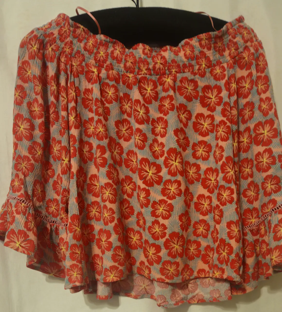 Blusa off shoulder con estampado floral en tonos rojos y amarillos. Diseño con volados en mangas y cintura elástica. Ideal para un look fresco y veraniego.