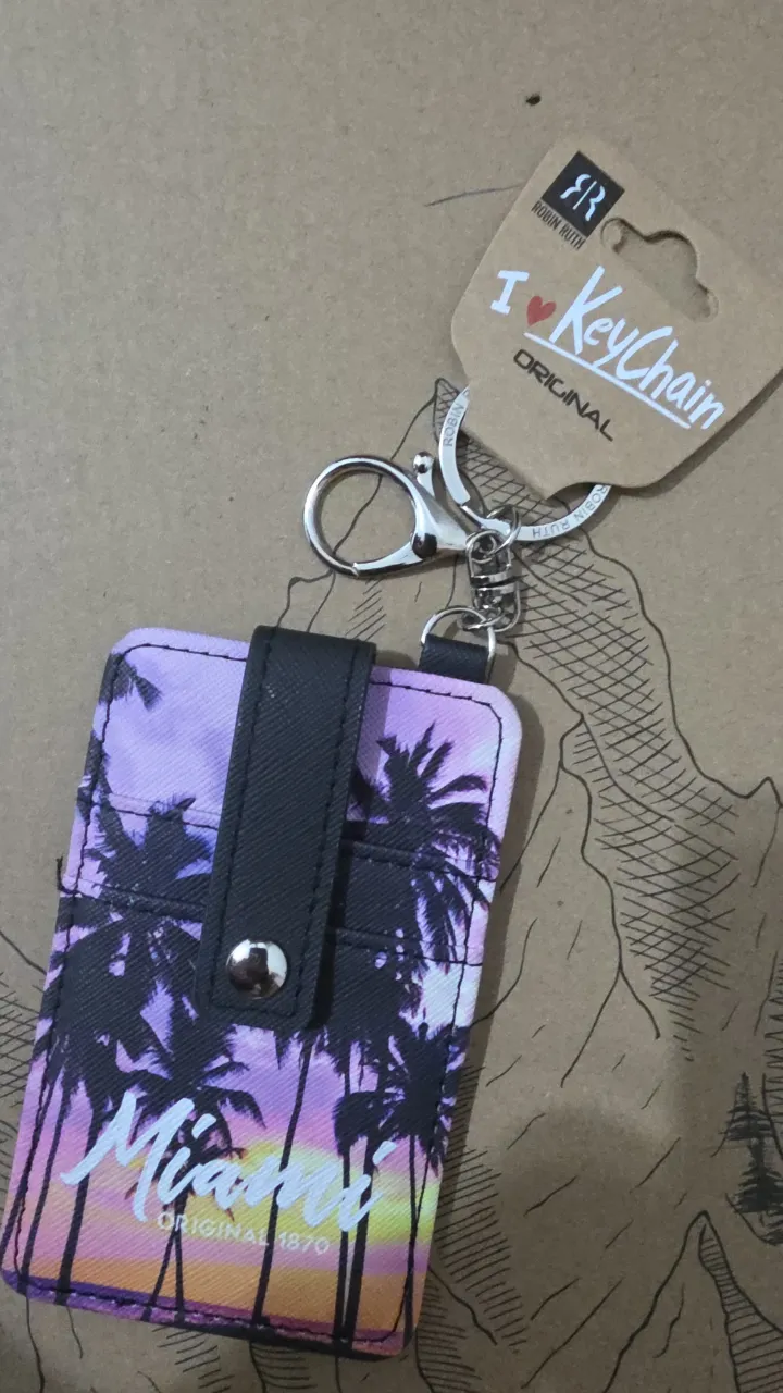 Porta credencial con llavero y diseño de palmeras y atardecer en Miami. El reverso es negro con ranuras para tarjetas.