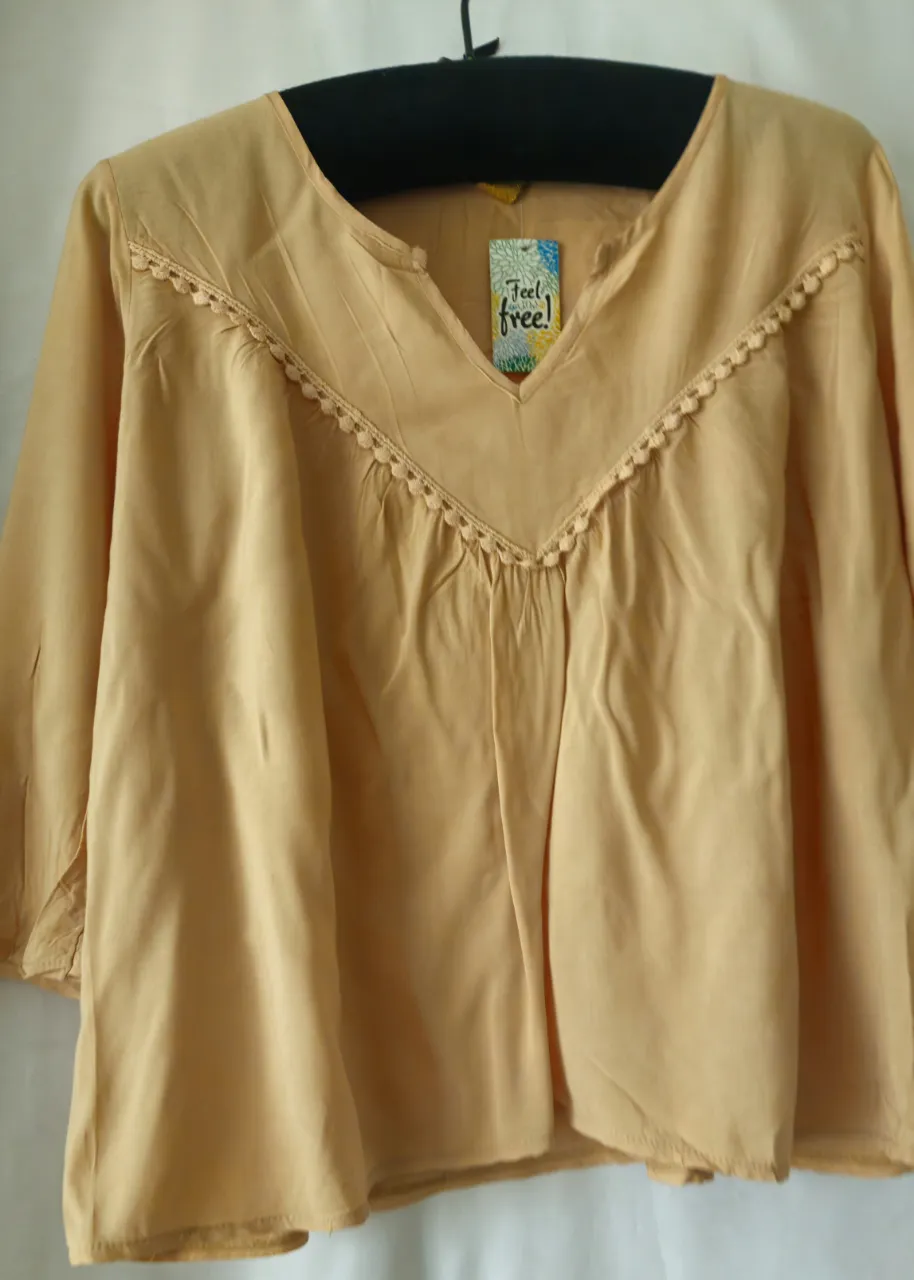 Blusa de color beige claro con detalles de encaje en el cuello y mangas 3/4. Ideal para un look casual y fresco.