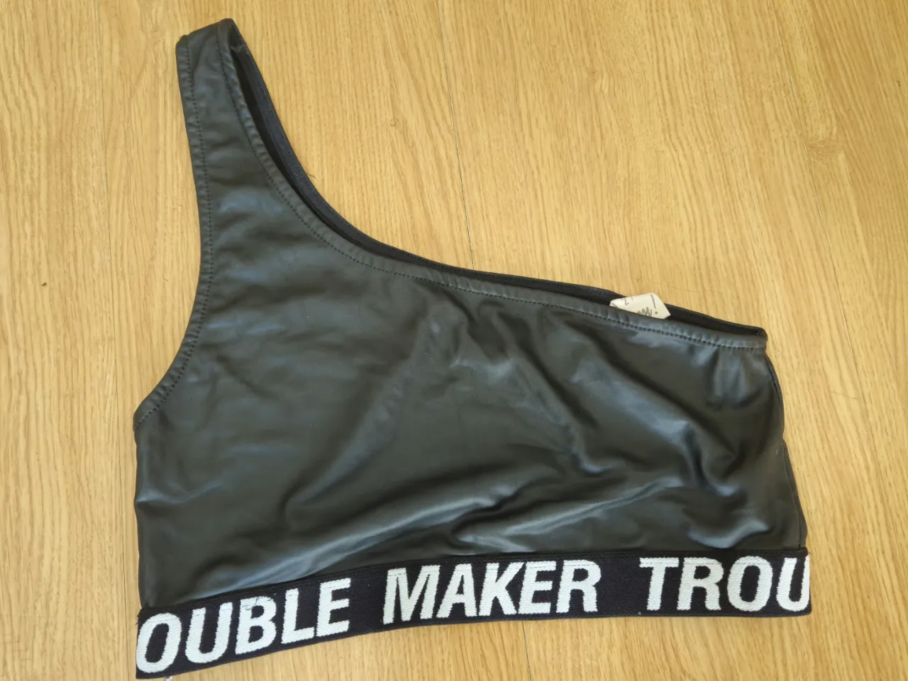 Top deportivo negro con un solo hombro y detalle de la marca "DOUBLE MAKER TROU" en la cintura. Ideal para un look moderno y audaz.