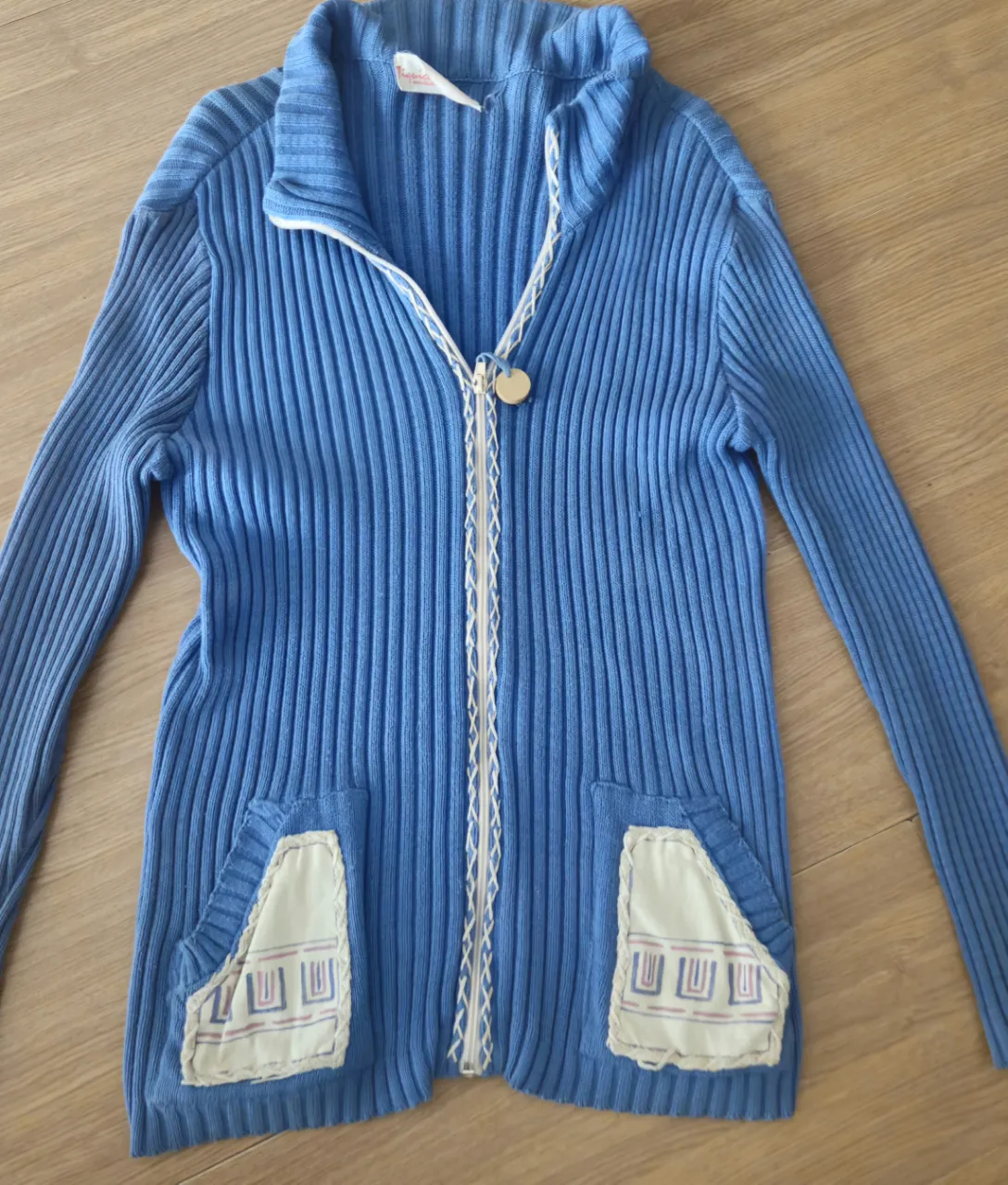 Sweater de tejido grueso azul con cierre y bolsillos. Detalles en blanco y diseño retro.