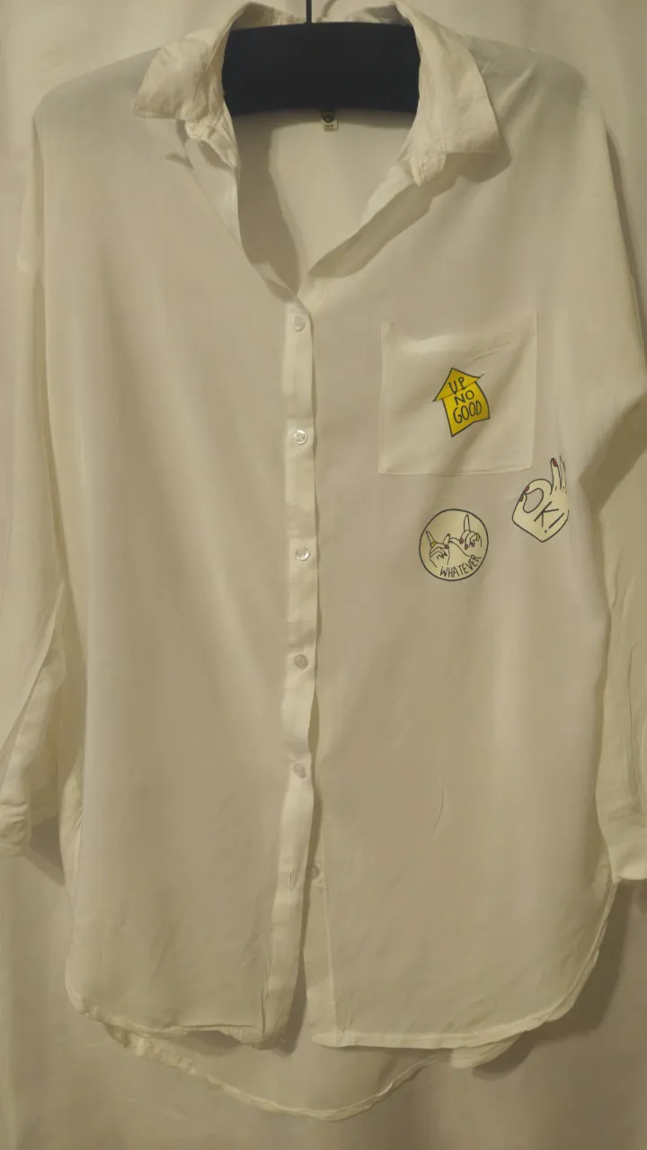 Camisa blanca de manga larga con detalles de estampados en el frente. Posee un bolsillo en el pecho y botones frontales. Ideal para un look casual y moderno. Sisa a sisa 44 cm, largo 70 cm.