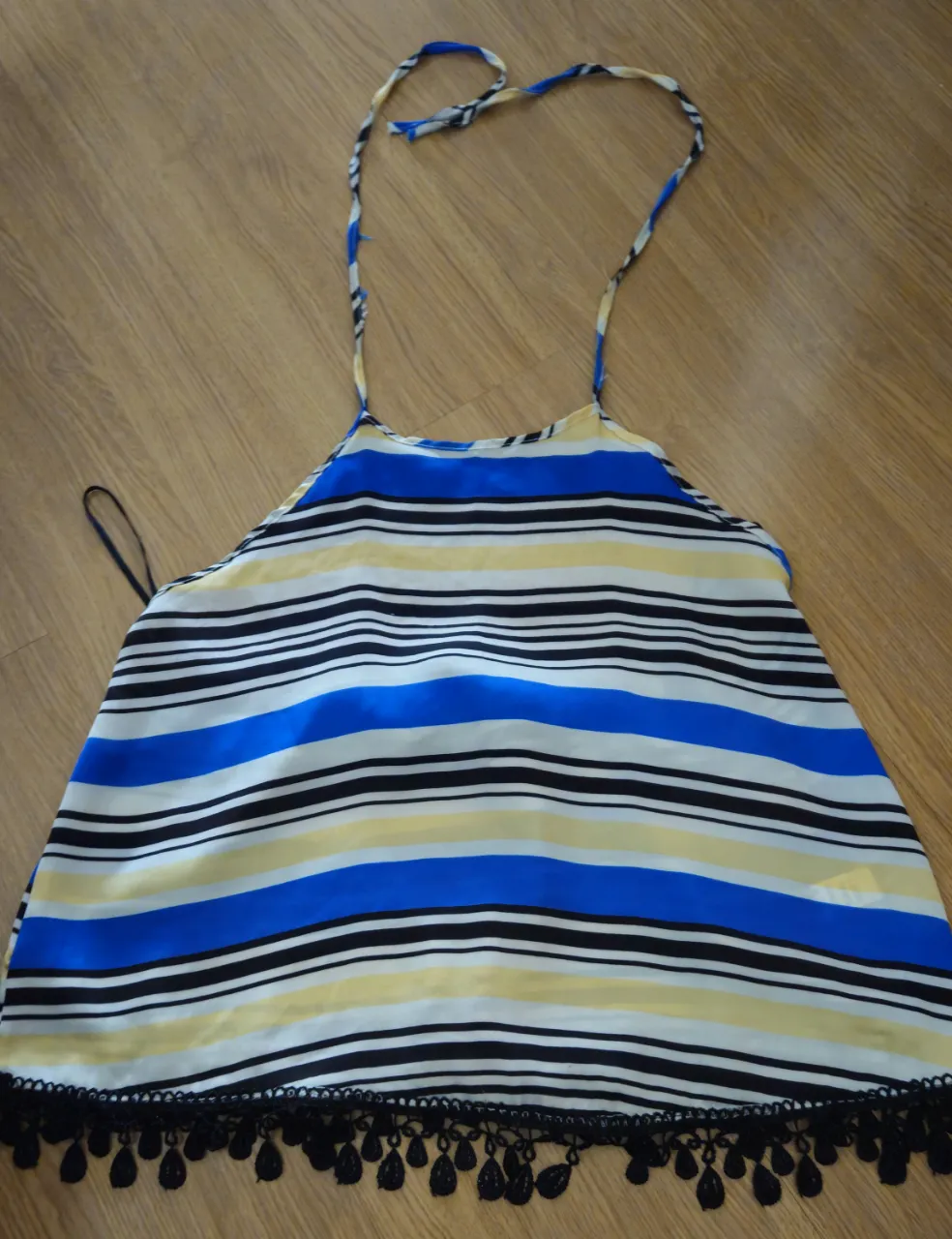 Top estampado a rayas multicolor con detalles de pompones negros en el ruedo. Ideal para un look fresco y divertido.