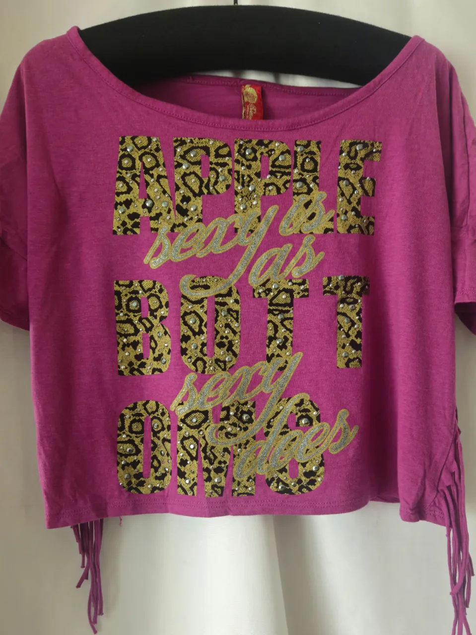 Remera crop fucsia con estampado  en letras doradas con detalles de brillos. Tiene flecos en los laterales.