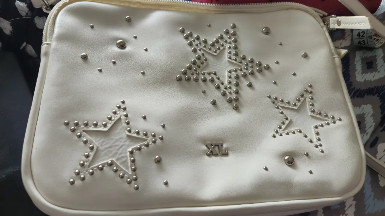 Bandolera beige con detalles de estrellas con tachas y apliques XL. Ideal para un look canchero y moderno. Medida 26*20, 3 divisiones y cierre interno, como nueva .