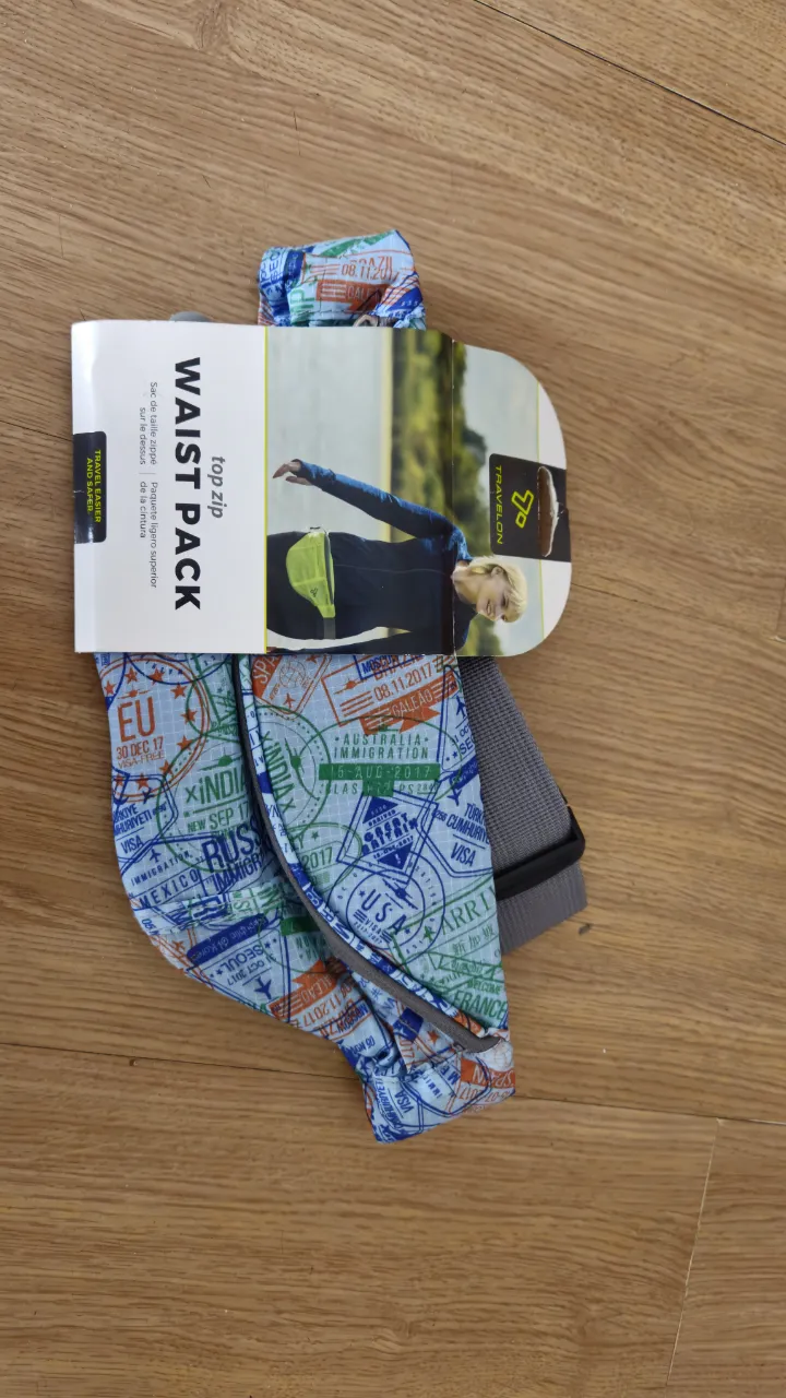 Riñonera Waist Pack top zip de la marca Travelon, ideal para viajes. Cuenta con un diseño estampado con sellos de pasaporte y un cinturón ajustable.