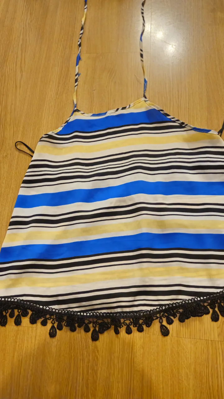 Top de mujer con estampado a rayas horizontales en amarillo, azul y negro. Tiene detalles de encaje negro en el borde inferior y tiras finas para atar al cuello. Ideal para el verano.
