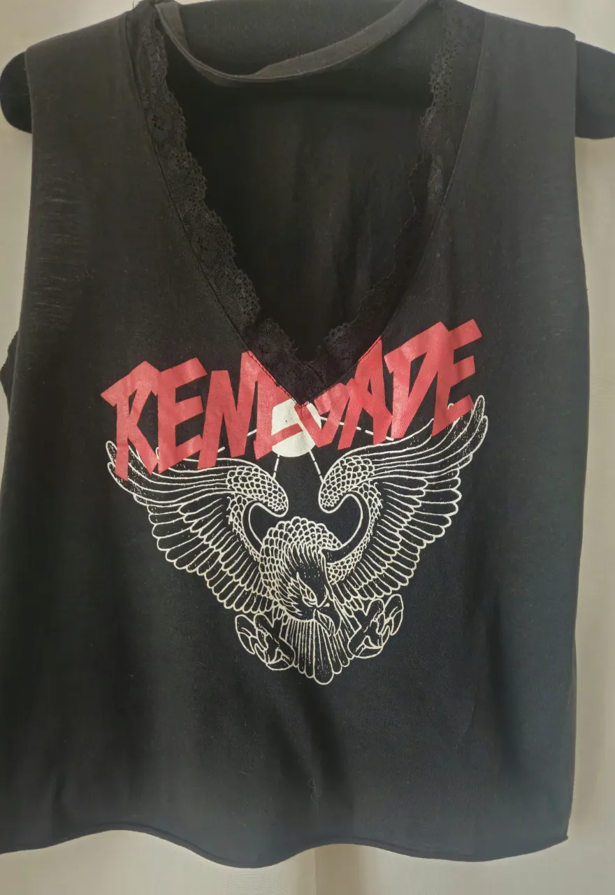 Musculosa negra con escote en V y detalles de encaje. Estampado "RENEGADE" en rojo y un diseño de águila con alas. Ideal para un look rocker y casual.