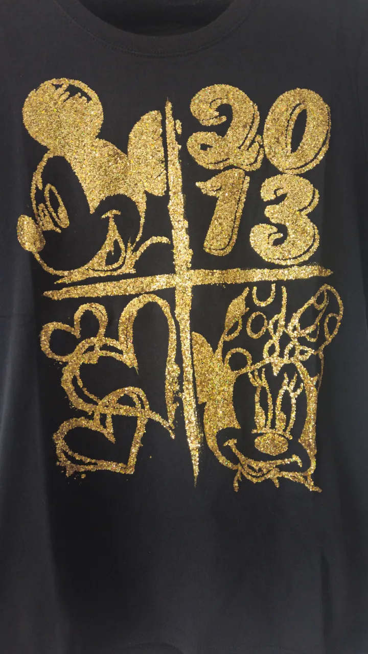 Remera negra de algodón con diseño dorado de Mickey y Minnie Mouse, con el número 2013. Ideal para un look casual y divertido.