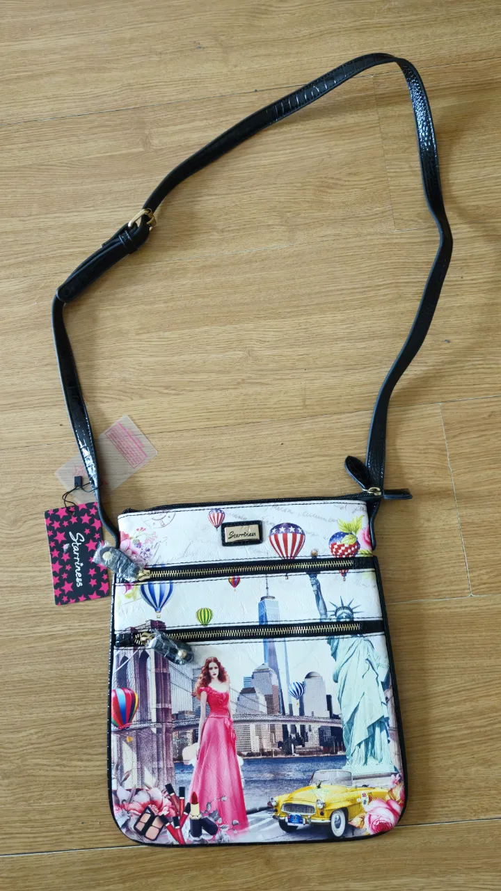 Bandolera con estampado de Nueva York, con detalles de cremalleras y correa ajustable. Ideal para un look casual y moderno. Medida 32*28 cm .