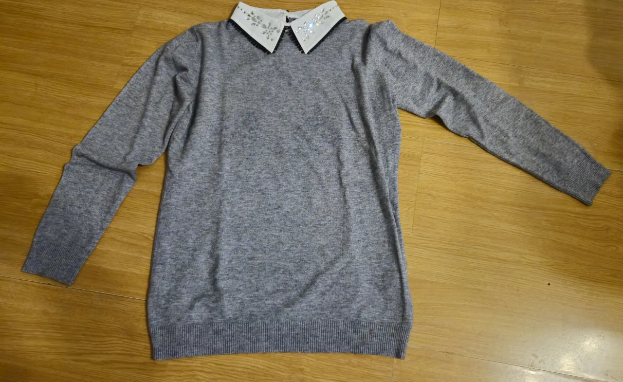 Sweater gris de cuello en V con cuello blanco adornado con detalles brillantes. Ideal para un look elegante y versátil.