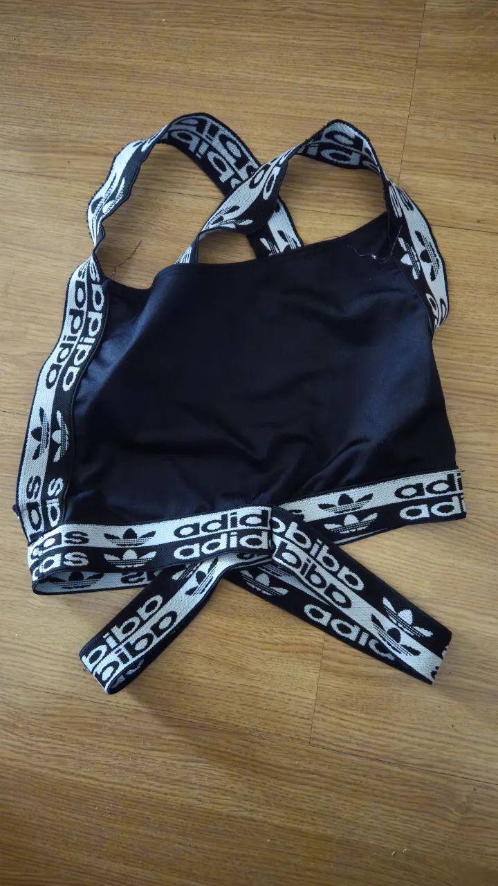 Top deportivo Adidas negro con tiras cruzadas y logo de la marca en blanco. Ideal para entrenar con estilo. No original.