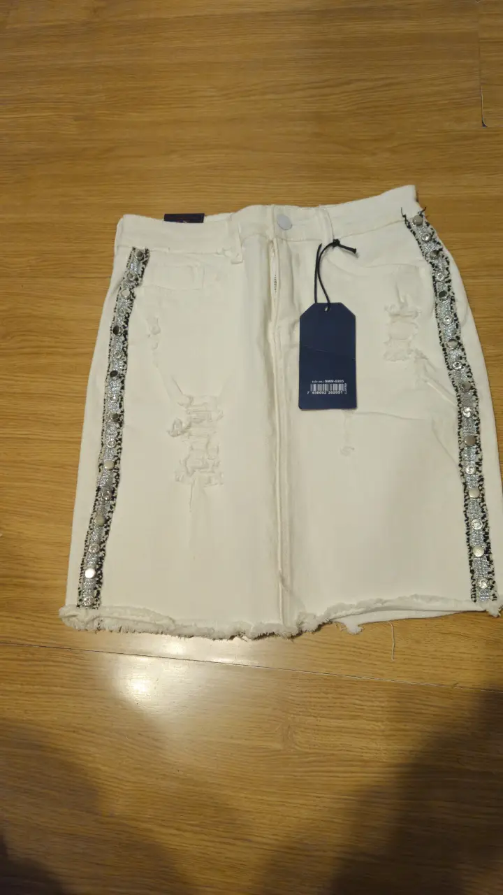 Minifalda de jean blanca con detalles rotos y apliques de strass en los laterales. Ideal para un look canchero y moderno.