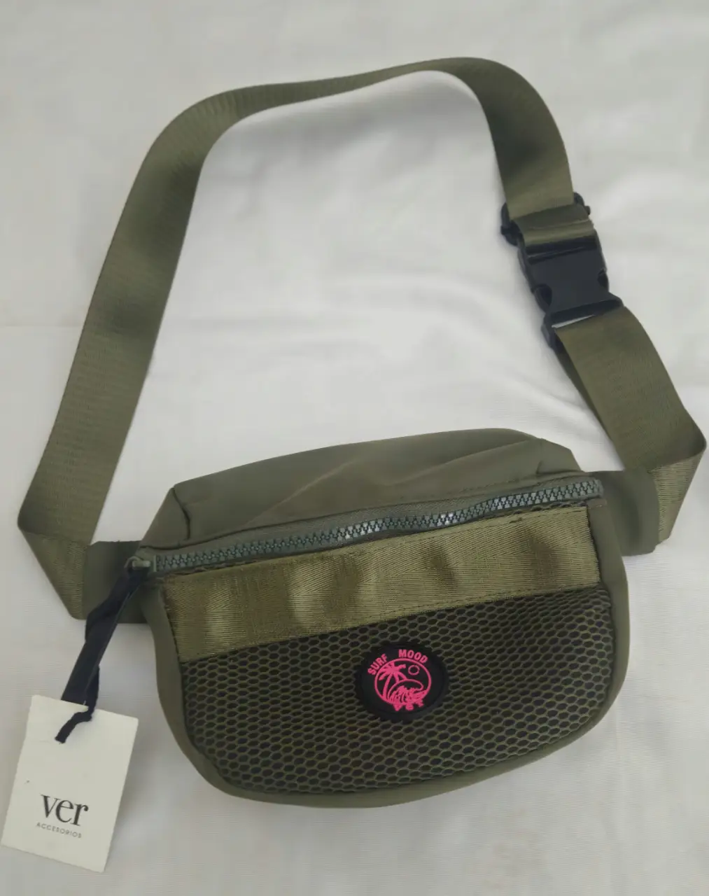 Riñonera verde militar con detalles en verde más claro y malla. Tiene un parche con un diseño en rosa. Ideal para llevar tus esenciales con estilo y comodidad.