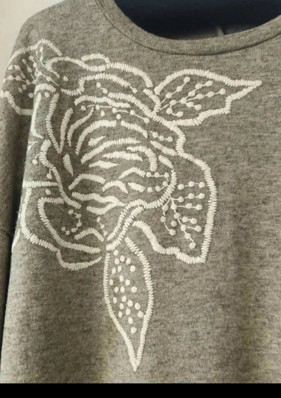 Buzo de cuello redondo gris con bordado floral blanco en el frente. Ideal para un look casual y cómodo.