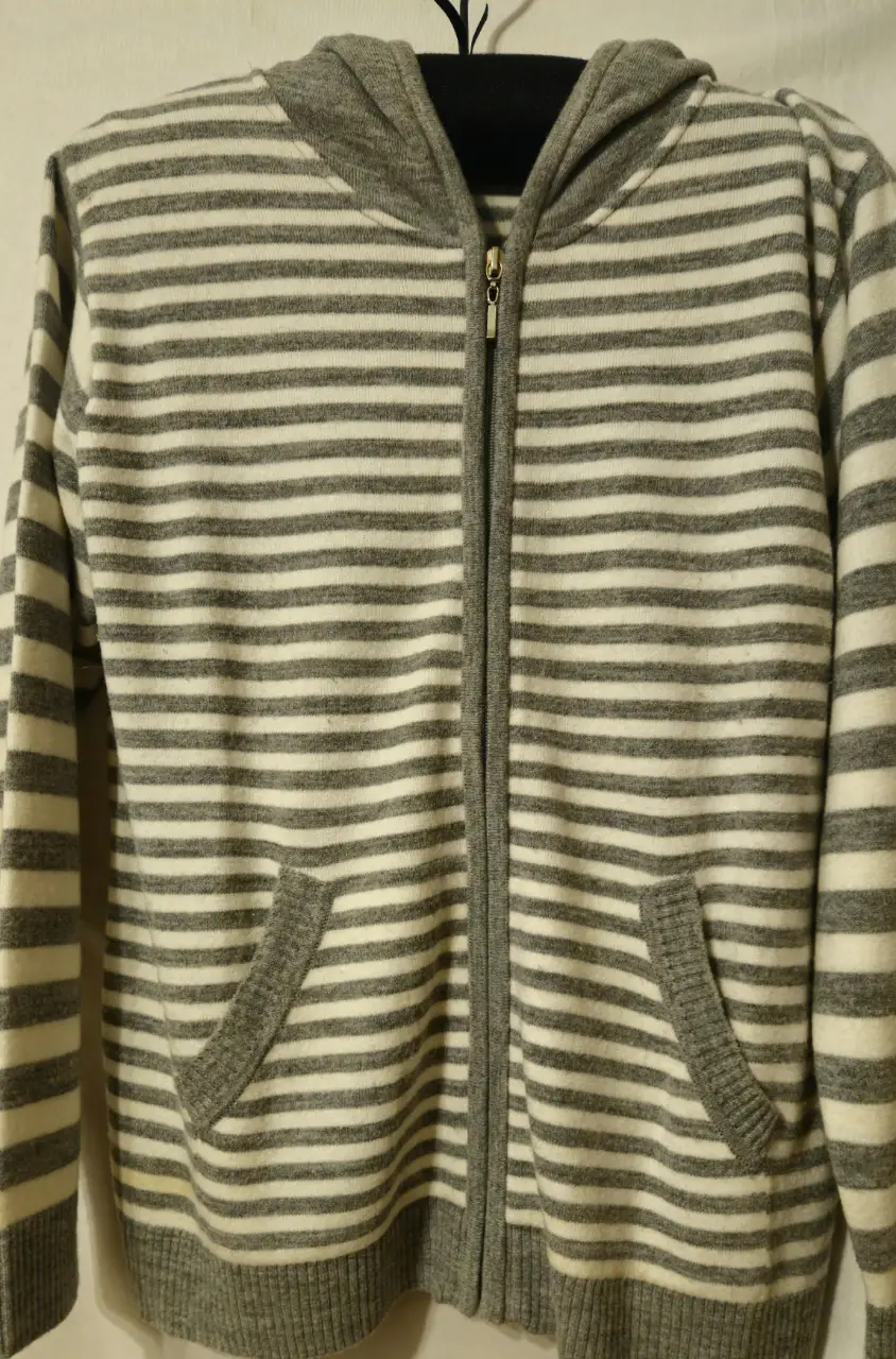 Buzo con cierre y capucha a rayas grises y blancas. Tiene bolsillos delanteros y un cierre frontal. Ideal para un look casual y cómodos Excelentes estado.