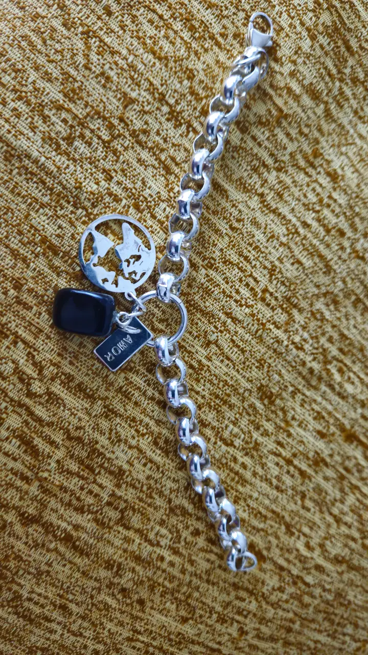 Pulsera de acero plateado con dijes. Incluye un dije circular con diseño y un dije rectangular con la inscripción "AMOR".