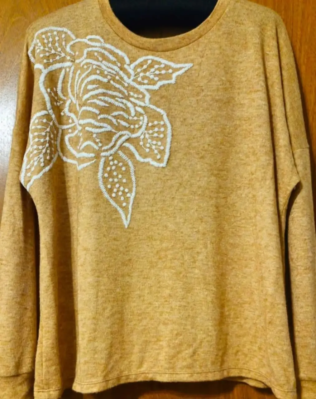 Sweater de cuello redondo color mostaza con bordado floral blanco en el frente. Ideal para un look casual y cómodo.