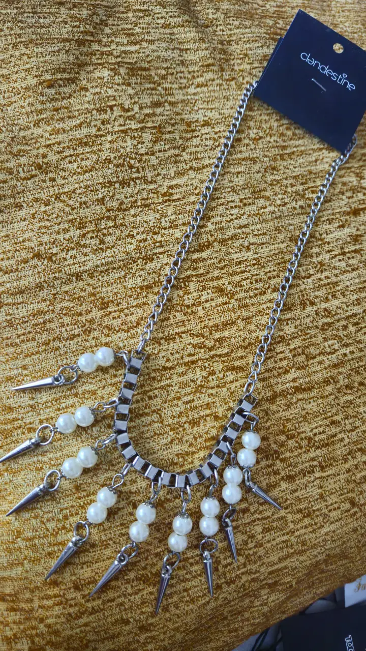 Collar plateado con cadena y dijes de perlas y pinchos. Ideal para darle un toque rockero y sofisticado a cualquier look.
