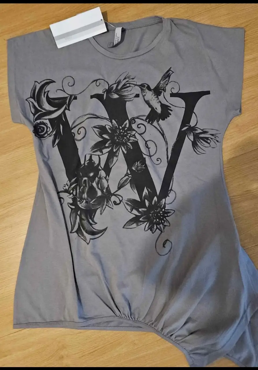 Remera gris con estampado de la letra 'W' adornada con flores y un colibrí. Ideal para un look casual y con estilo.
