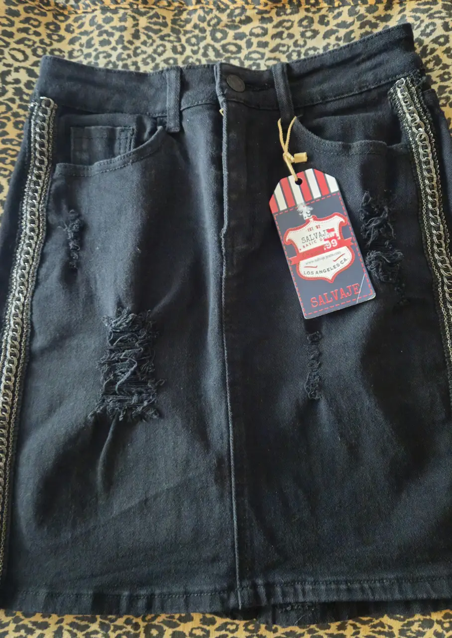 Minifalda de jean negra con detalles rotos y cadenas plateadas en los laterales. Ideal para un look casual y moderno.