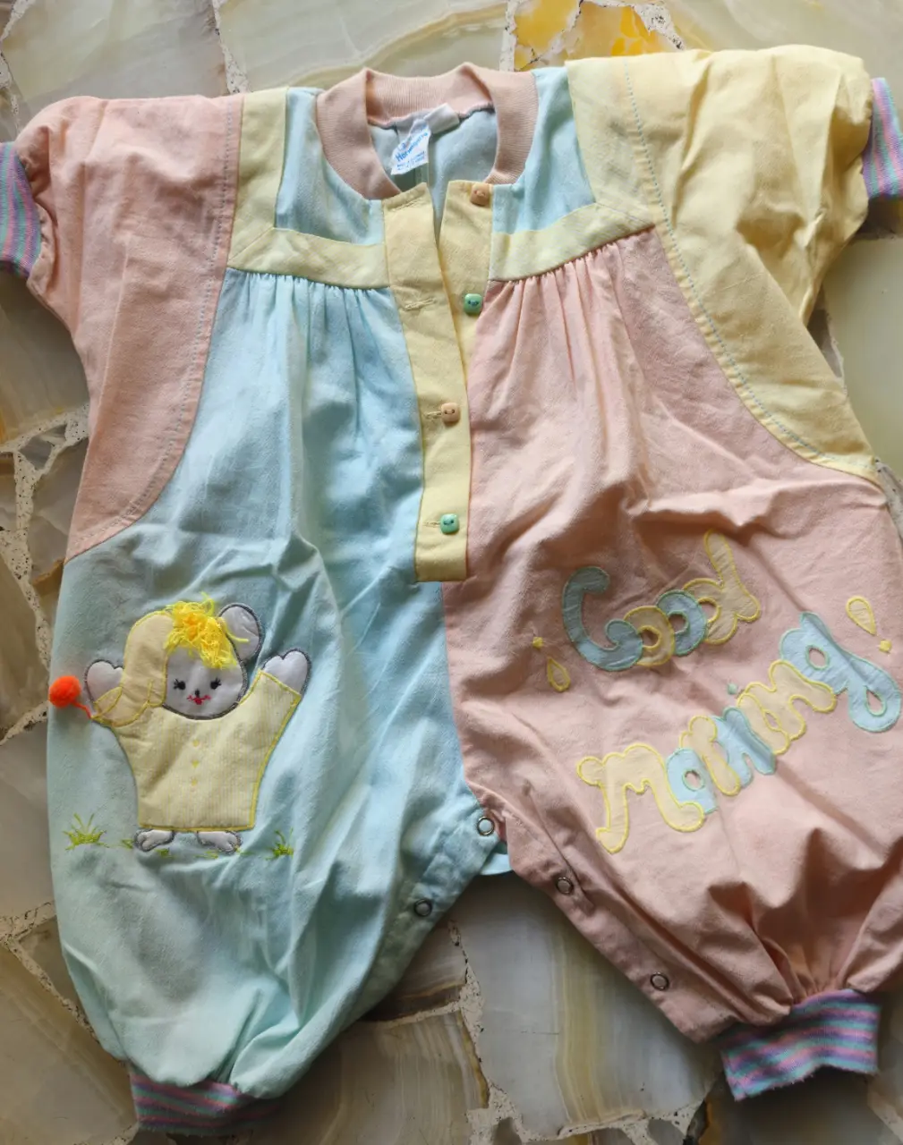Mono corto de bebé, con diseño patchwork en tonos pastel. Cuenta con un aplique de un oso y la frase "Good Morning" bordada. Ideal para un look cómodo y tierno.