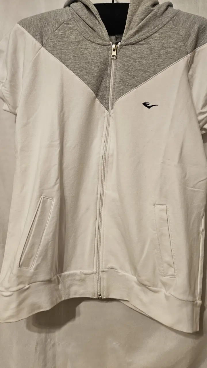 Buzo con cierre y capucha, manga corta, blanco con detalles en gris. Ideal para un look deportivo y casual.