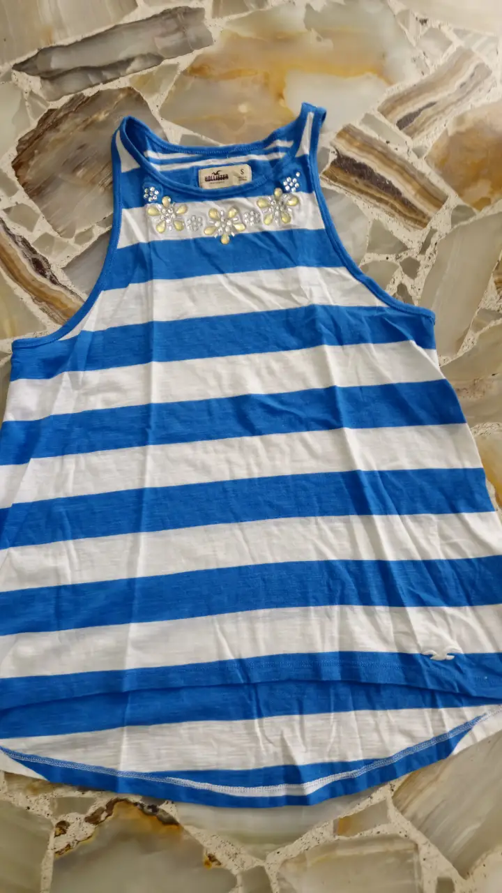 Musculosa de mujer Hollister a rayas azules y blancas, con detalles de flores en el cuello. Ideal para un look casual y fresco.