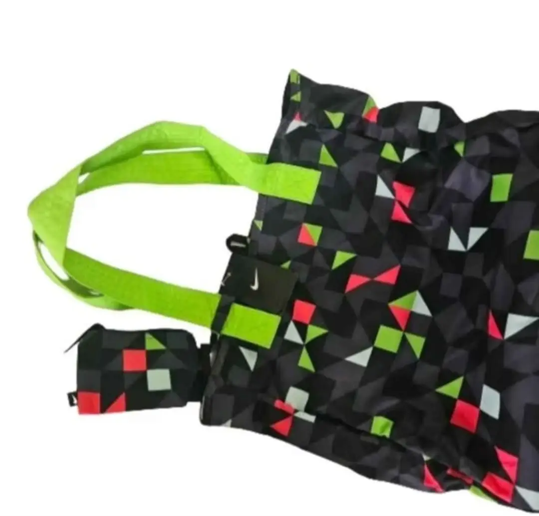 Bolso tote Nike con estampado geométrico en tonos grises, rojos y verdes. Asas y detalles en verde neón. Incluye un pequeño monedero a juego.