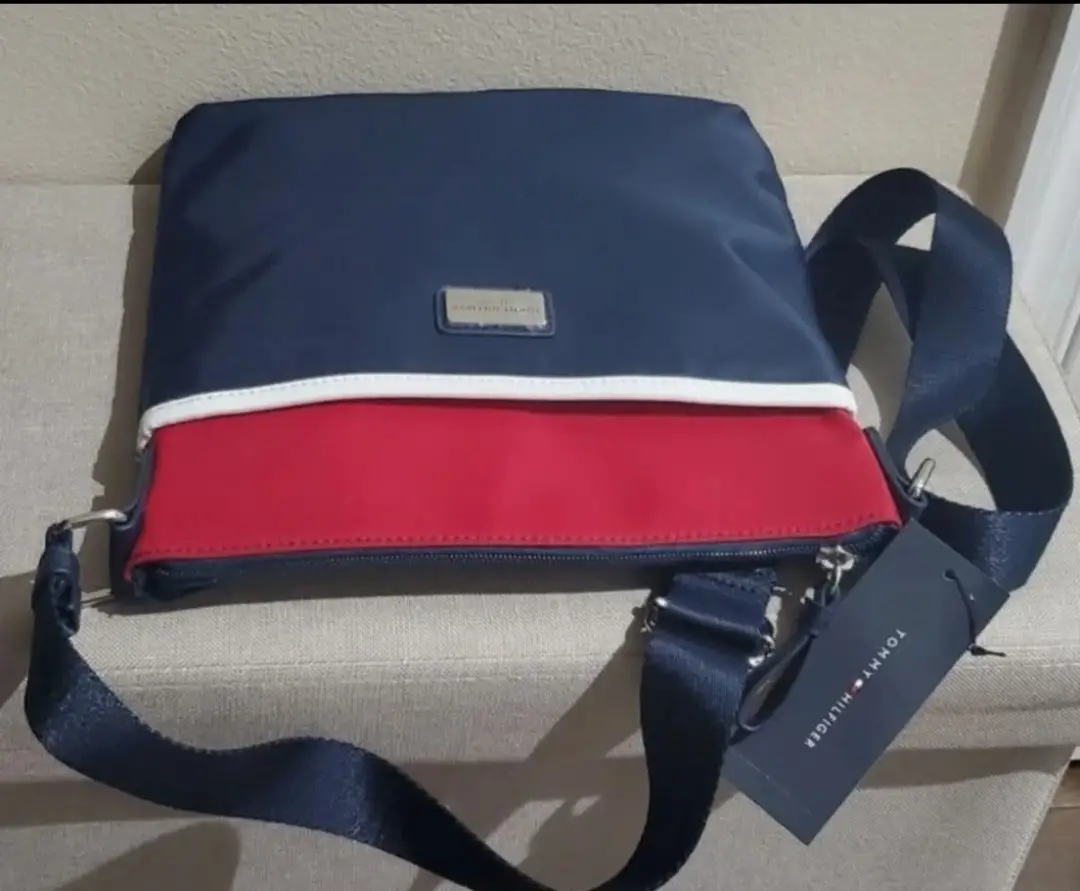 Bandolera Tommy Hilfiger en color azul marino con detalles en rojo y blanco. Ideal para llevar tus esenciales con estilo y comodidad. Perfecta para un look casual y moderno.