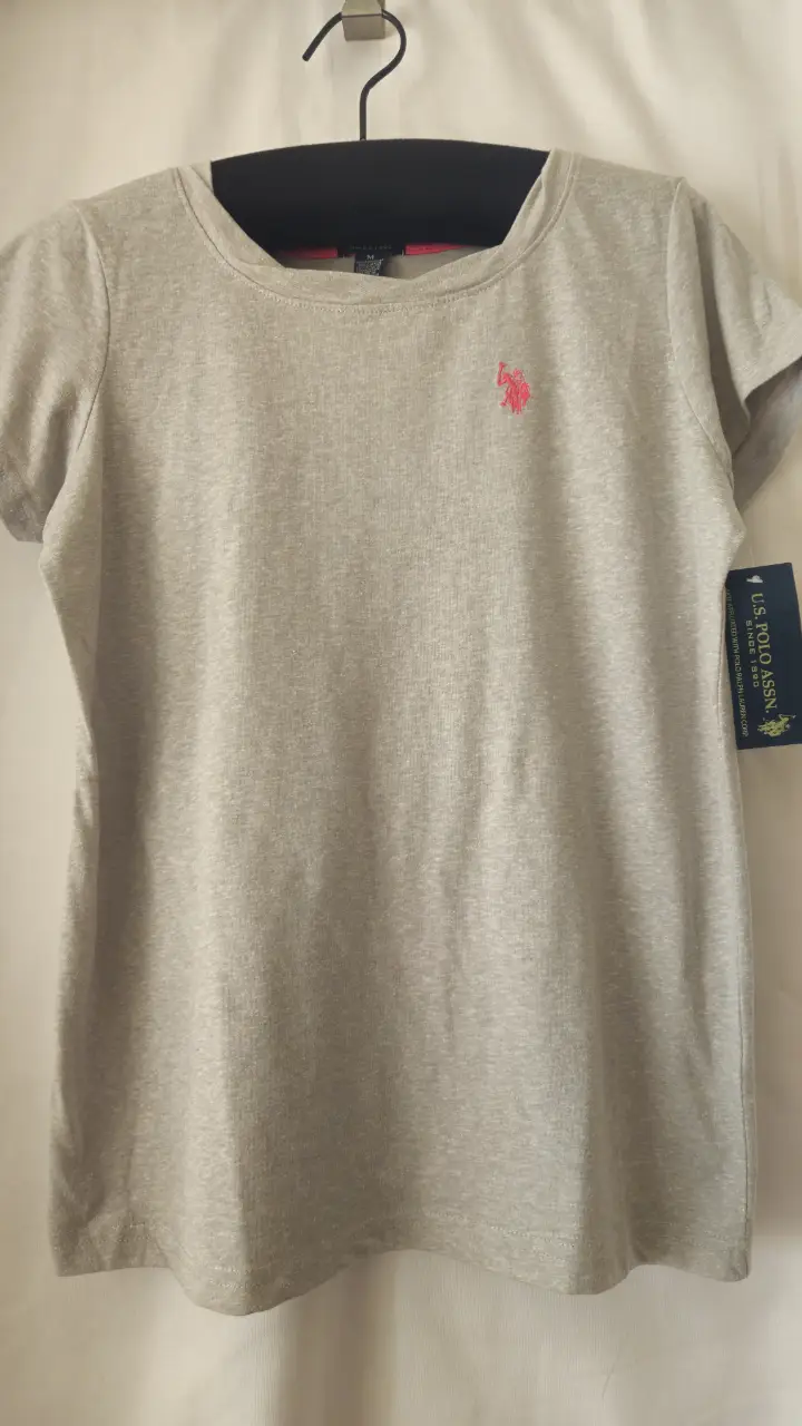 Remera de mujer US Polo Assn. de manga corta, color gris claro con logo rosa en el pecho. Ideal para un look casual y cómodo.