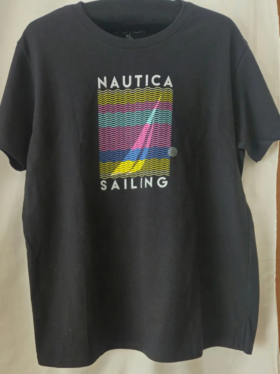 Remera negra de mujer con estampado "NAUTICA SAILING" en el frente. Diseño con olas en colores vibrantes. Ideal para un look casual y moderno.