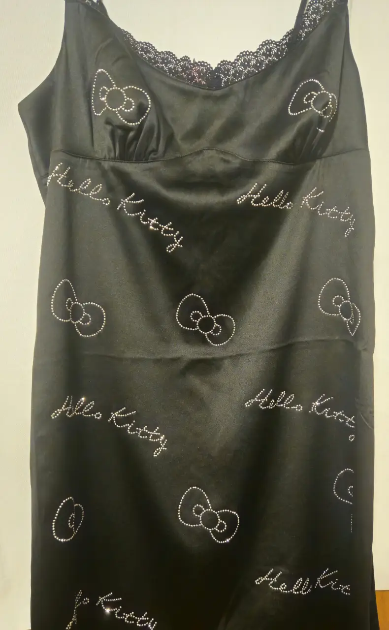 Vestido mini negro de satén con tirantes finos, detalles de Hello Kitty con brillantes y encaje en el escote. Ideal para fiestas y salidas.
