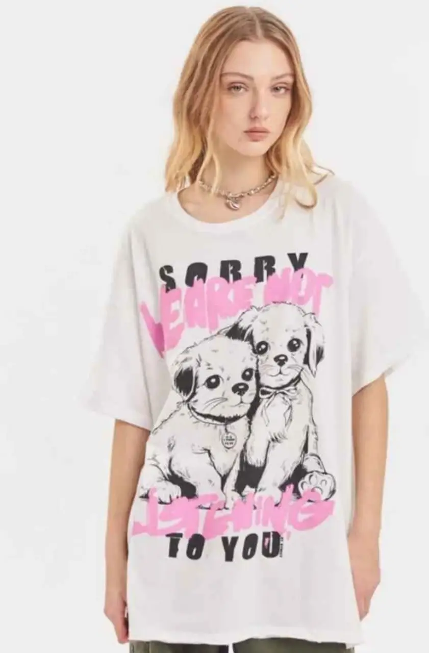 Remera blanca de algodón con estampado de dos cachorros y la frase "SORRY WE ARE NOT LISTENING TO YOU" en rosa. Ideal para un look casual y moderno.