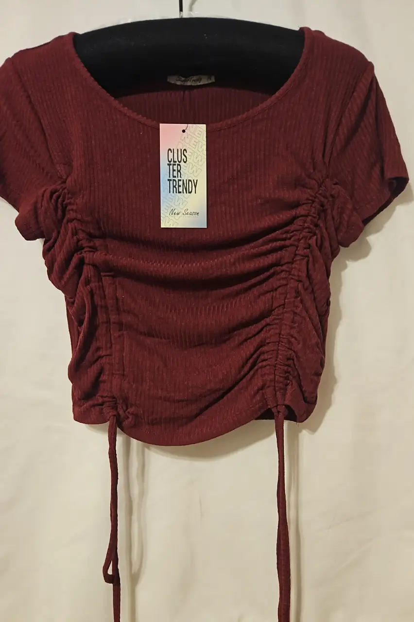 Top de mujer color borgoña con fruncidos laterales y detalle de lazos ajustables. Ideal para un look moderno y versátil.
