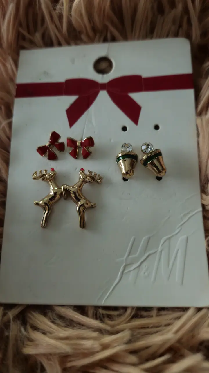 Set de aros de H&M con diseño navideño. Incluye tres pares: dos pares de aros con forma de reno y un par de aros con forma de campana con detalles brillantes y moños rojos.