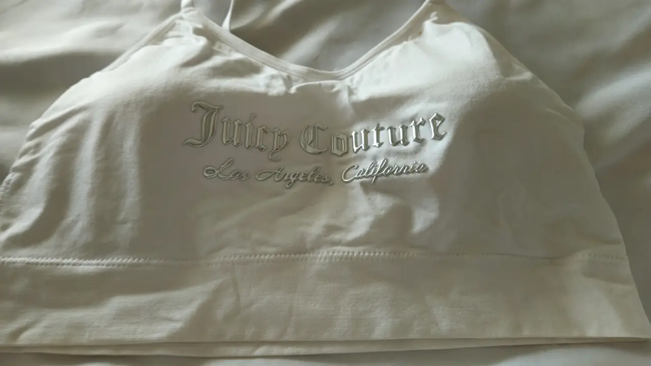 Top deportivo blanco de la marca Juicy Couture, con el logo bordado en plateado. Ideal para actividades de bajo impacto o para un look casual y cómodo.
