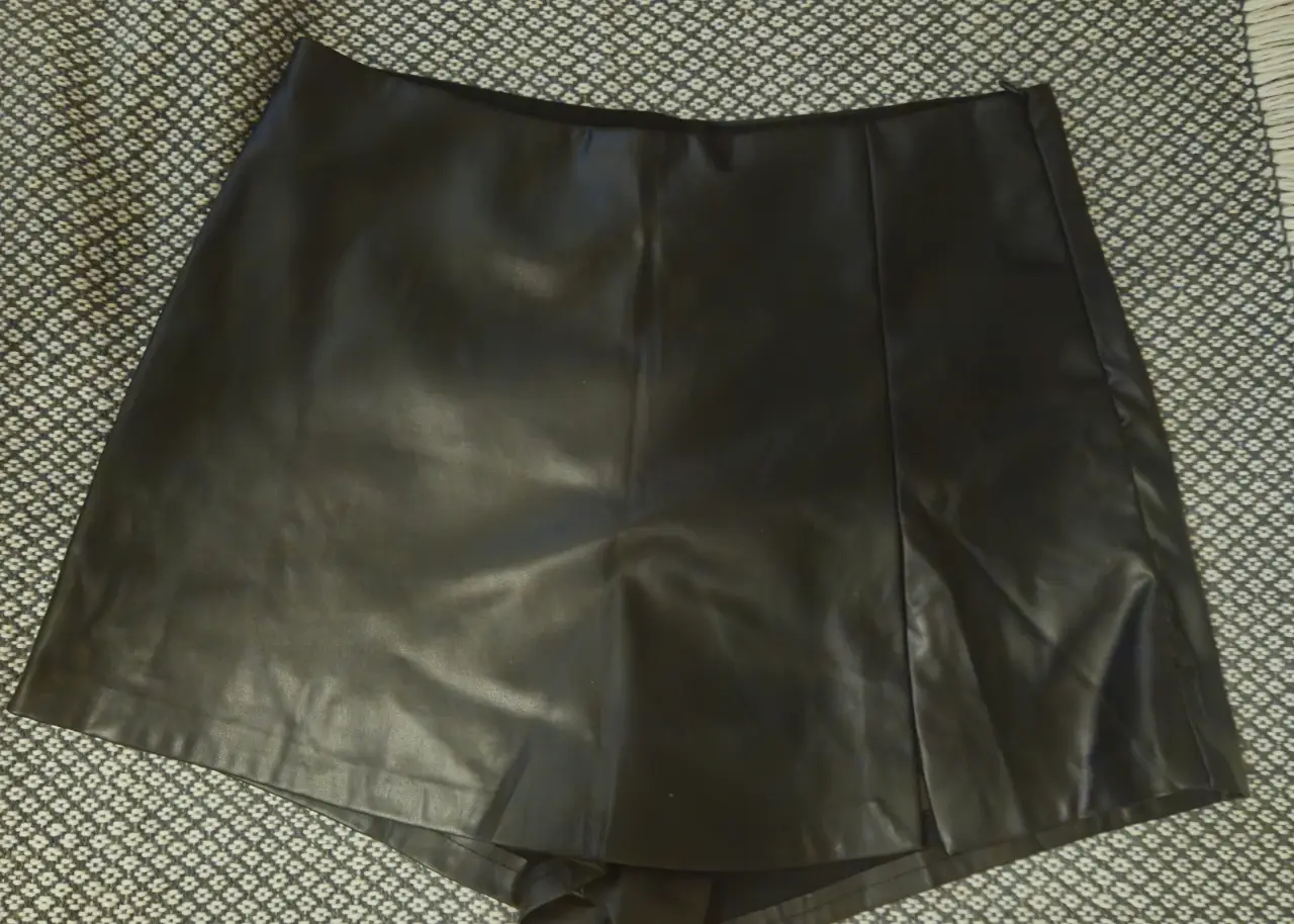 Short de cuero sintético negro tiro alto con detalle de abertura lateral. Ideal para un look moderno y sofisticado. Cintura 38 cm 