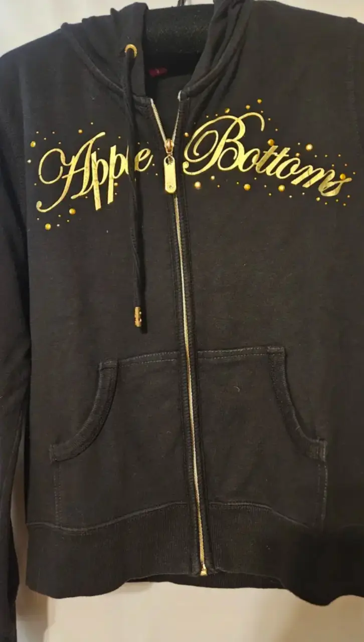 Buzo con cierre de la marca Apple Bottoms, color negro con detalles dorados. Talle XXL/TG. Ideal para un look casual y cómodo.