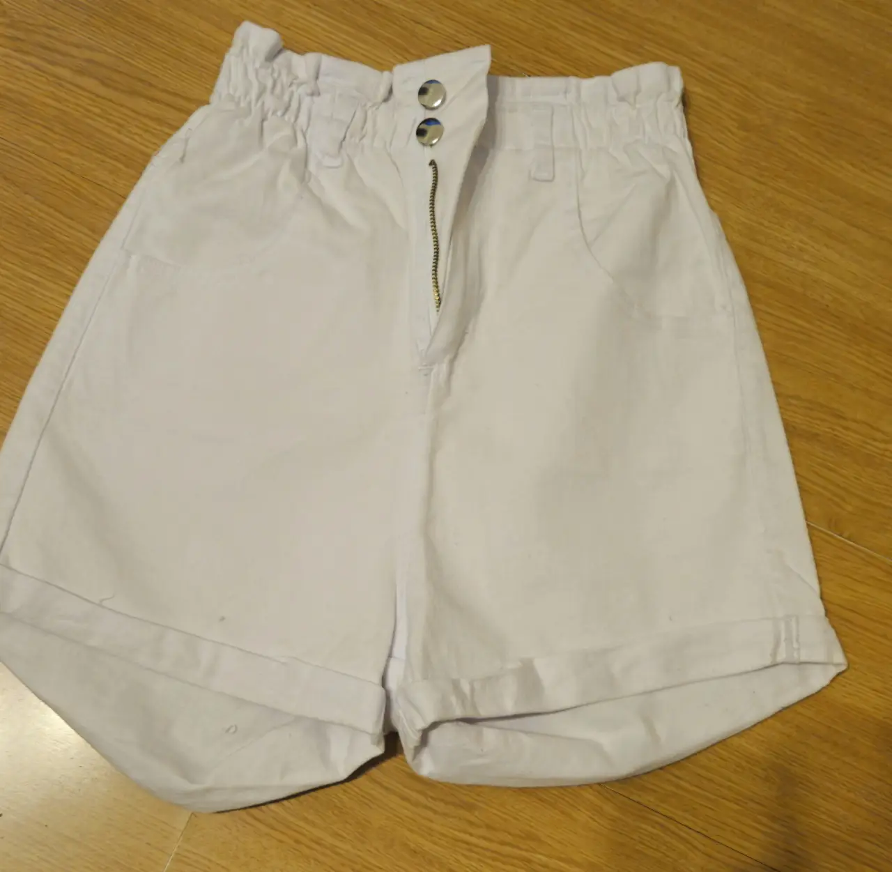 Shorts de mujer tiro alto, color blanco. Con cintura elastizada y botones. Ideal para un look casual y fresco.