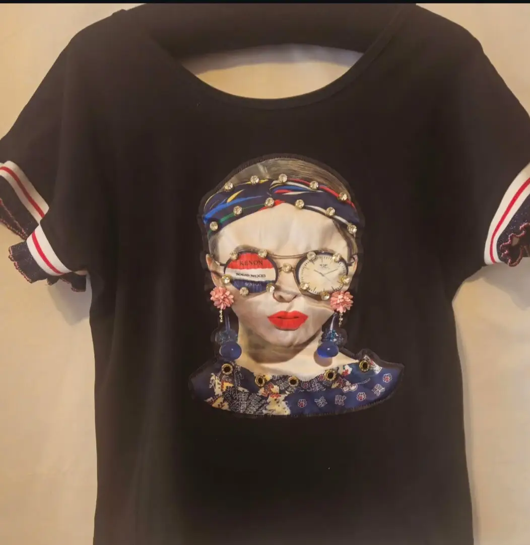 Remera negra con estampado de rostro femenino con detalles de anteojos y accesorios. Estilo moderno y llamativo, ideal para un look casual con un toque de originalidad.