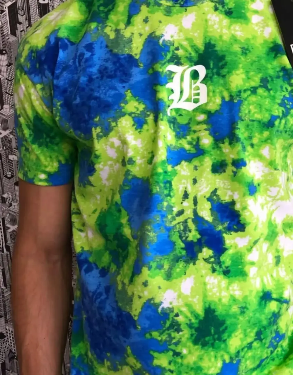 Remera de hombre con estampado tie dye en tonos verde y azul. Diseño con un logo "B" blanco en el pecho. Ideal para un look casual y moderno.