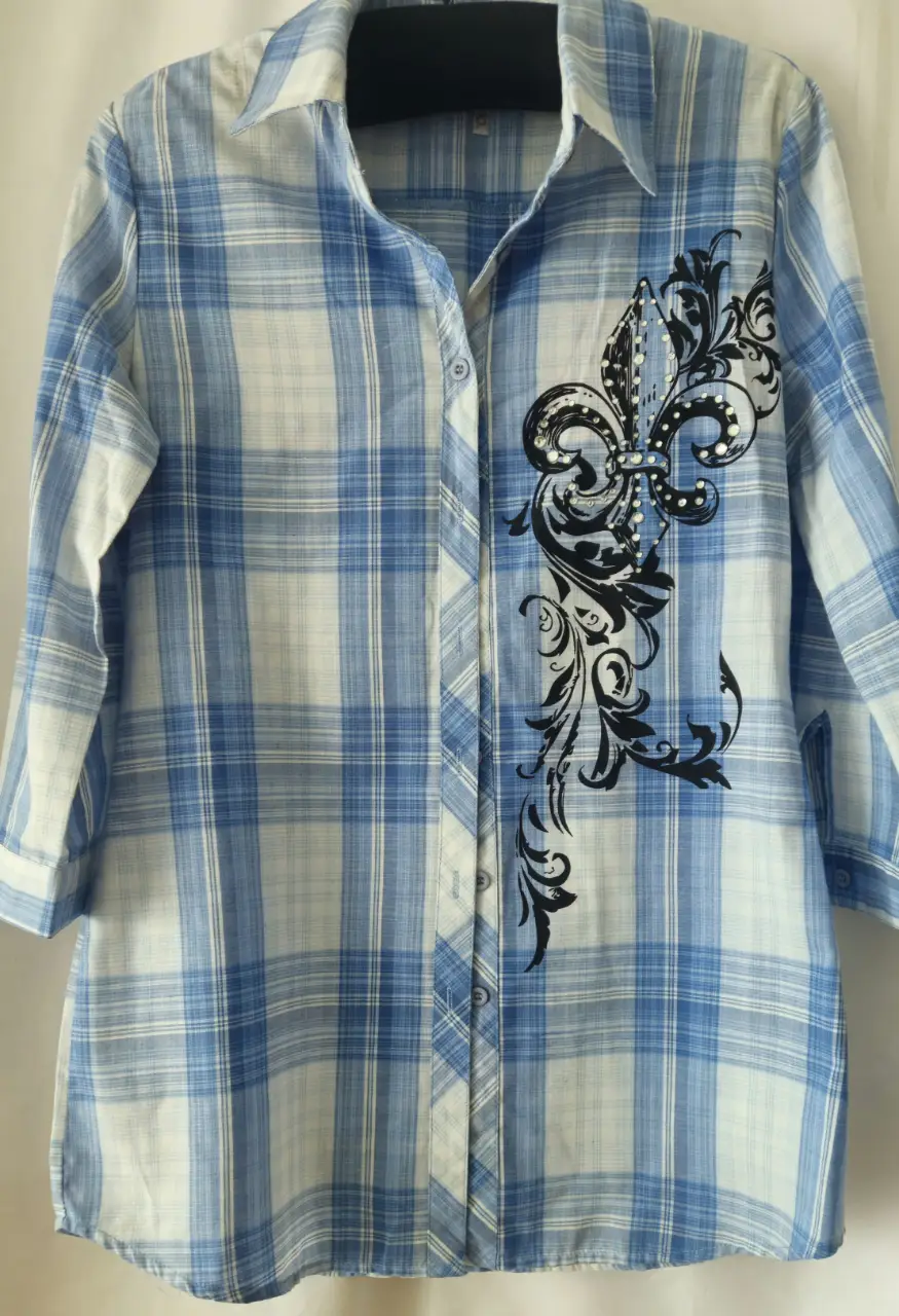 Camisa a cuadros azul y blanca de mujer, con detalle de diseño floral en el frente. Manga 3/4 y cuello clásico. Ideal para un look casual y fresco.