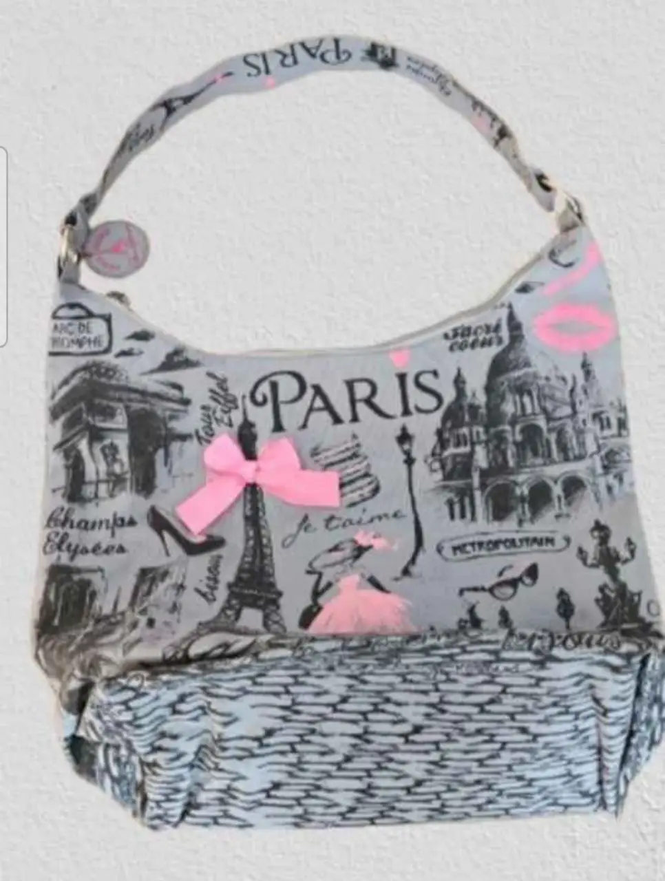 Cartera de hombro con diseño de París. Ideal para un look casual y urbano. Cuenta con un lazo rosa y detalles de la ciudad.